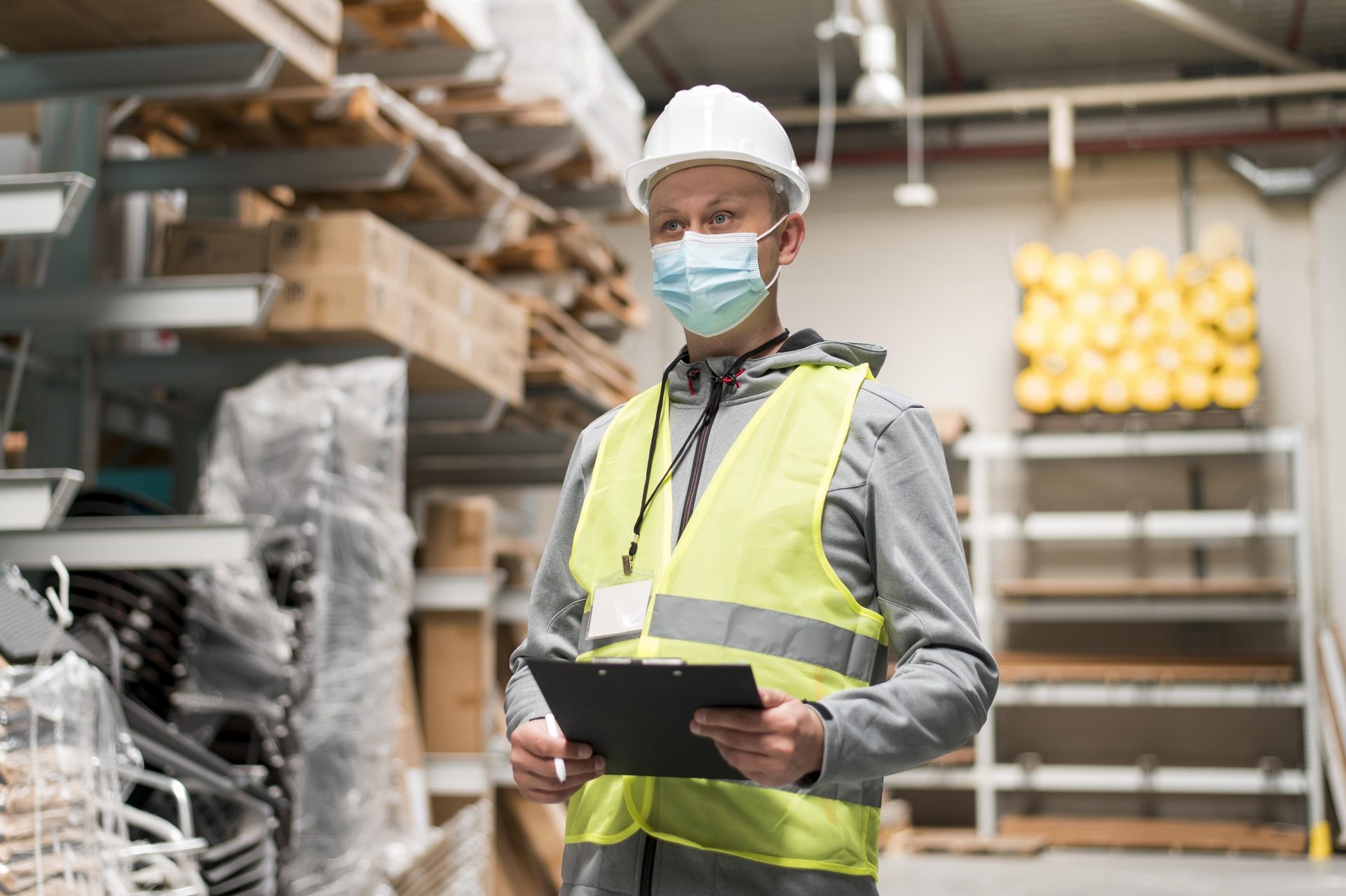 Responsable de seguridad con chaleco amarillo y casco blanco realizando una evaluación de riesgos en almacén industrial — principios generales de prevención